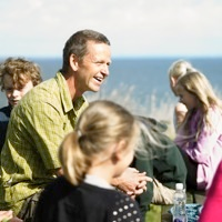 Smilende mand med børn, der opholder sig udendørs nær kysten.