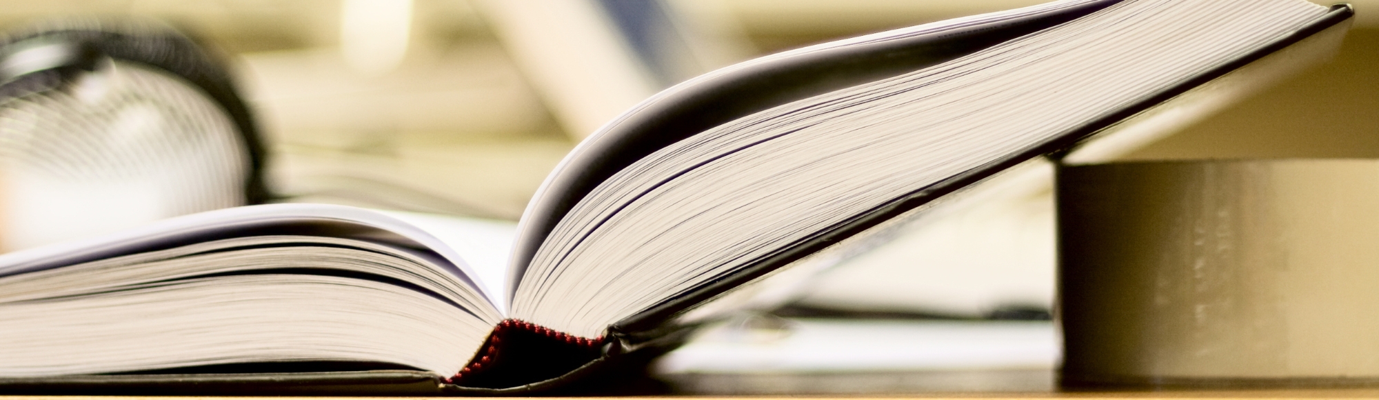 Close-up of an open hardcover book resting on a stack of books with visible pages.