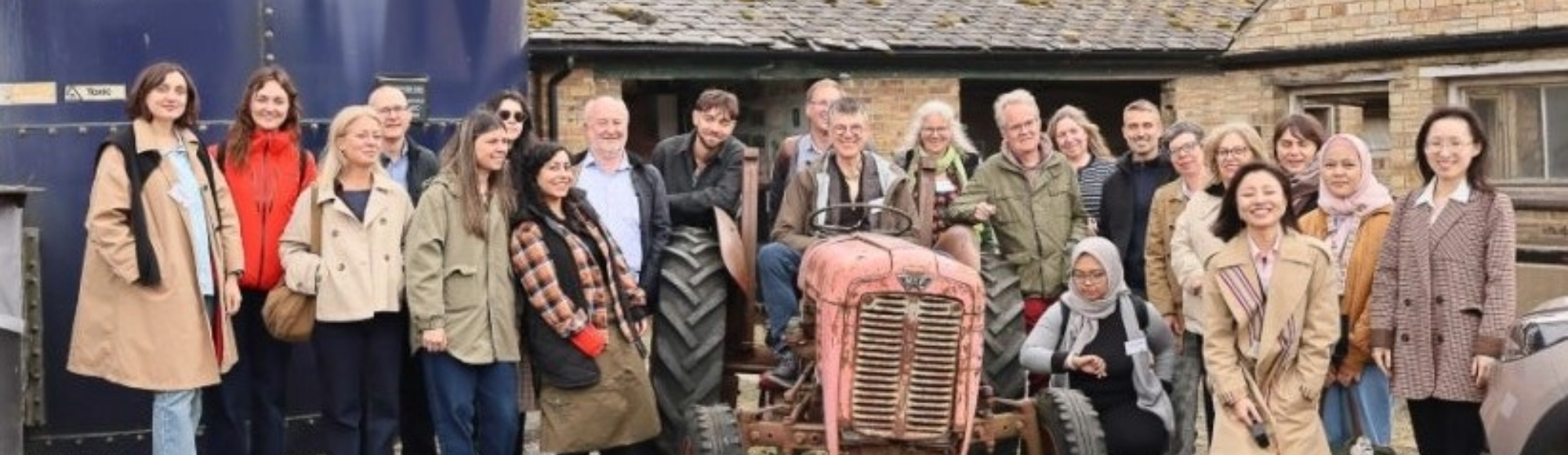Group of people standing and sitting around an old tractor outside farm buildings.