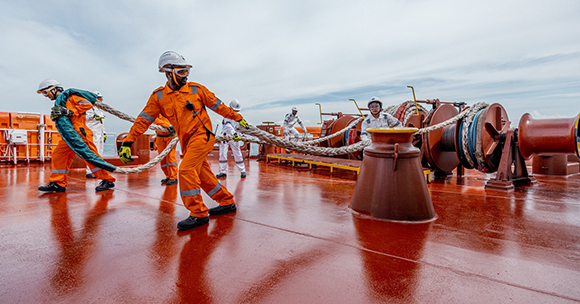 Billede af sømænd - mænd og kvinder - der arbejder på dækket af et stort fragtskib.
