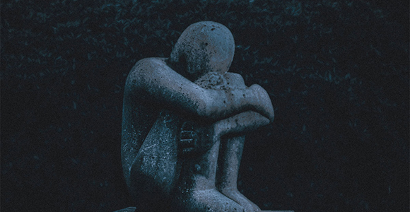 Statue af menneskefigur, der sidder ned med hovedet og armene begravet i sine knæ.