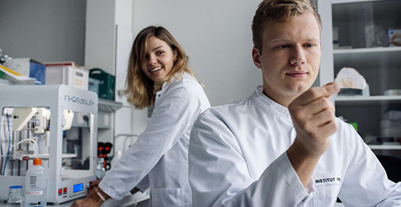 Billede af to forskere i hvide kitler, der kigger på et forskningsartefakt