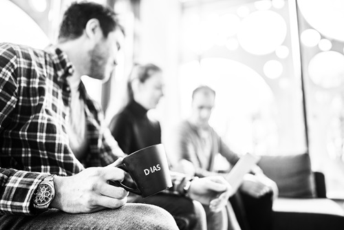 people drinking coffee together, one holding a cup with the DIAS logo on it