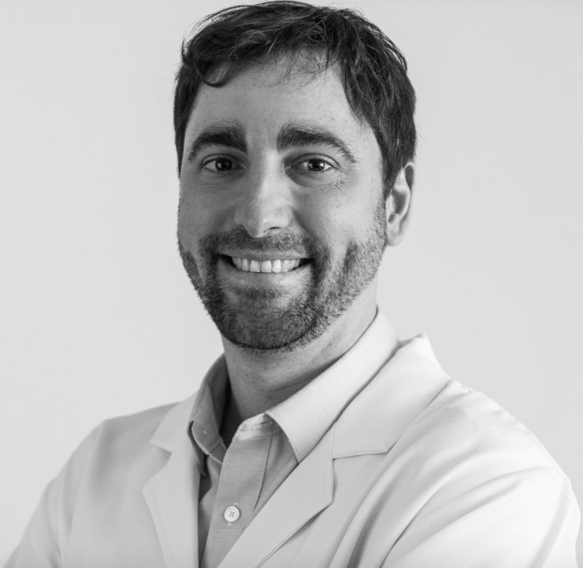 A black and white portrait of a person identified as Tiago da Silva Medina, wearing a light-colored lab coat over a collared shirt. The person has short, dark hair, and the background is plain and light-colored.