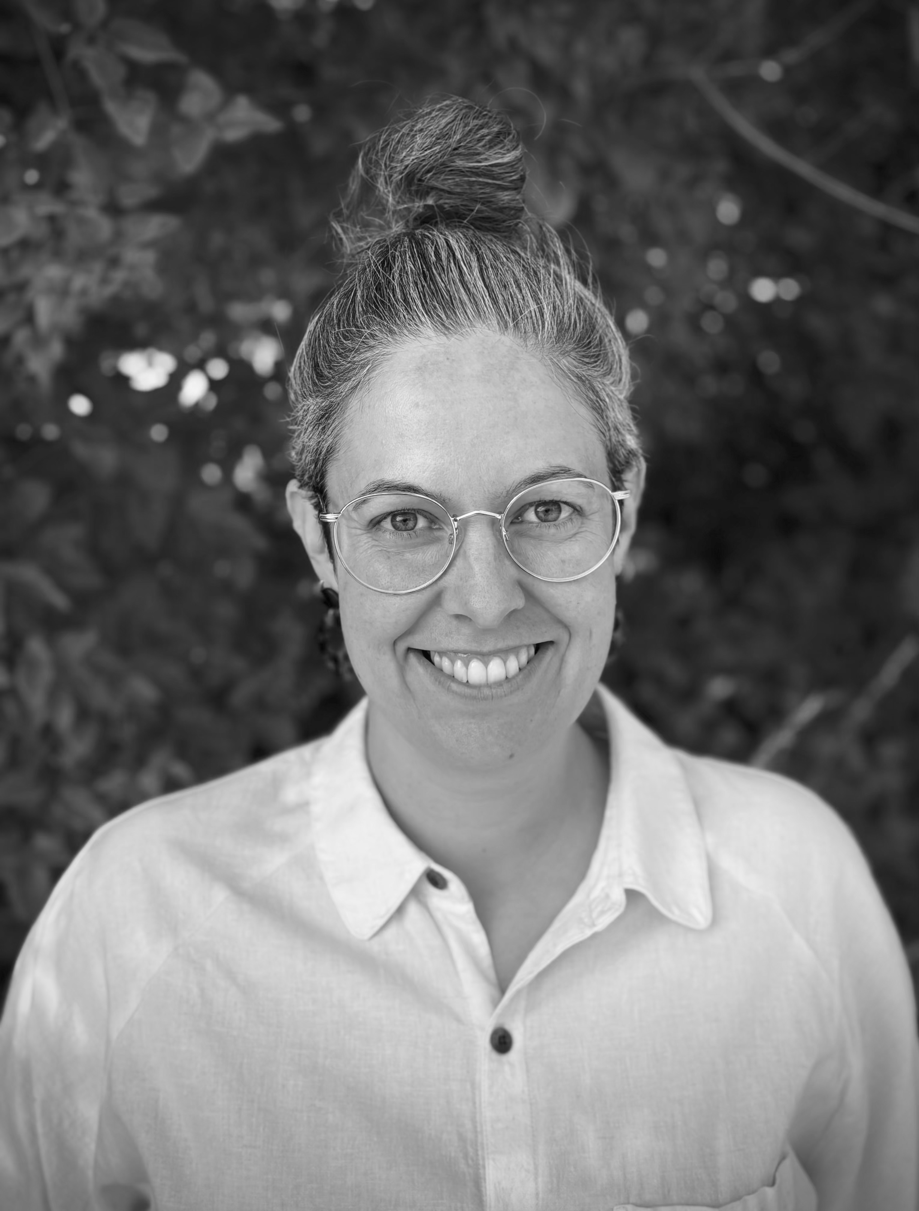 Portræt af Emily Cousins, visiting fellow hos DIAS i Odense, smilende og iført skjorte, med grønne blade i baggrunden.
