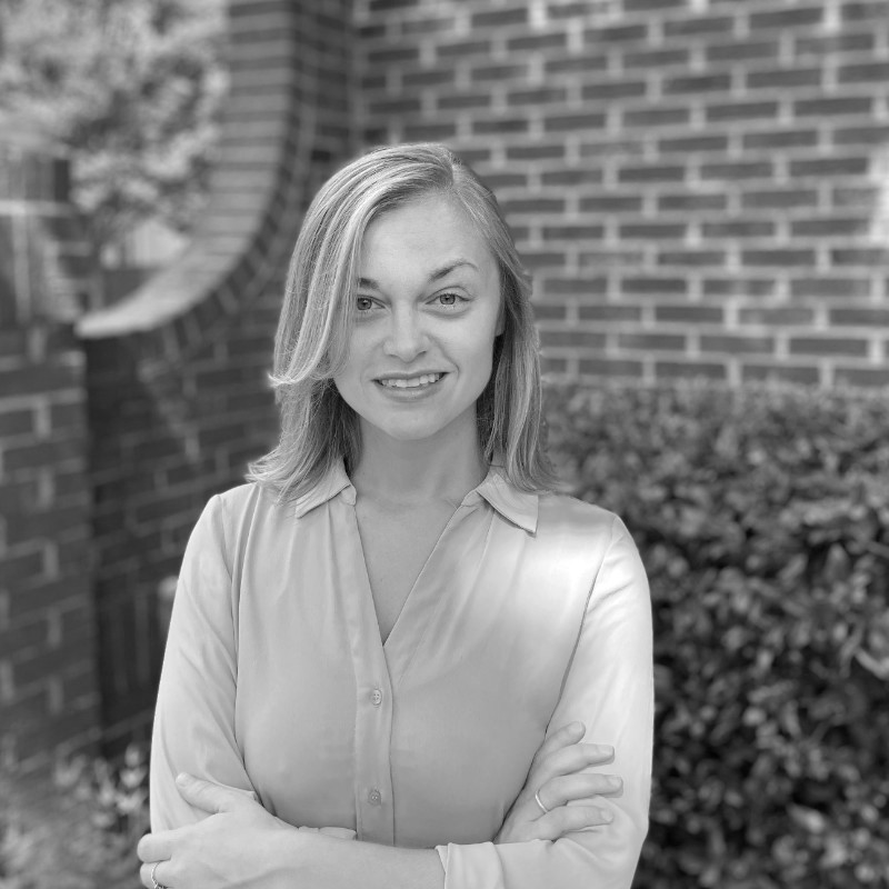 Kaitlin Alper, DIAS-alumne, står udendørs foran en murstensvæg med armene over kors og smiler til kameraet