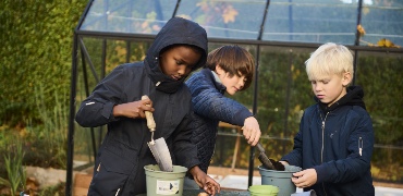 Tre børn arbejder med planter ved et drivhus
