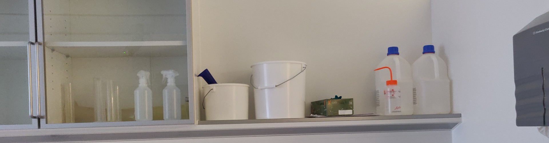 Skab og hylde med rengøringsudstyr, plastbeholdere og flasker.