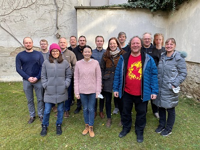 Group portrait of people standing outside on a lawn near a wall.