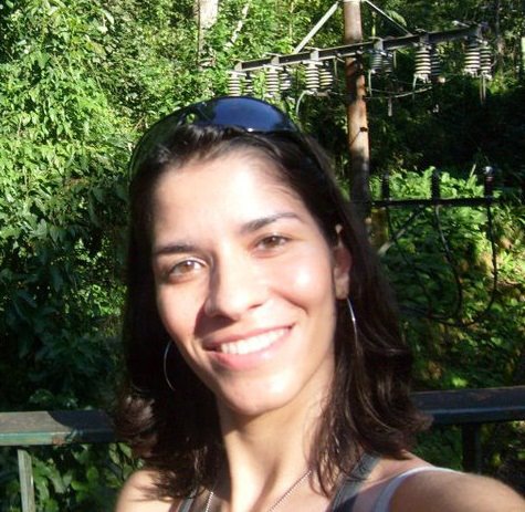 Natasha Jorge smiling outdoors with green foliage in the background.