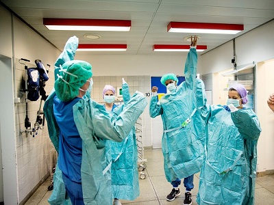Medical staff in blue protective gowns and masks celebrating in a hospital hallway.