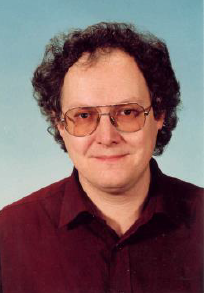 Head-and-shoulders portrait of Peter Florian Stadler wearing tinted glasses and a dark burgundy collared shirt against a light blue background.