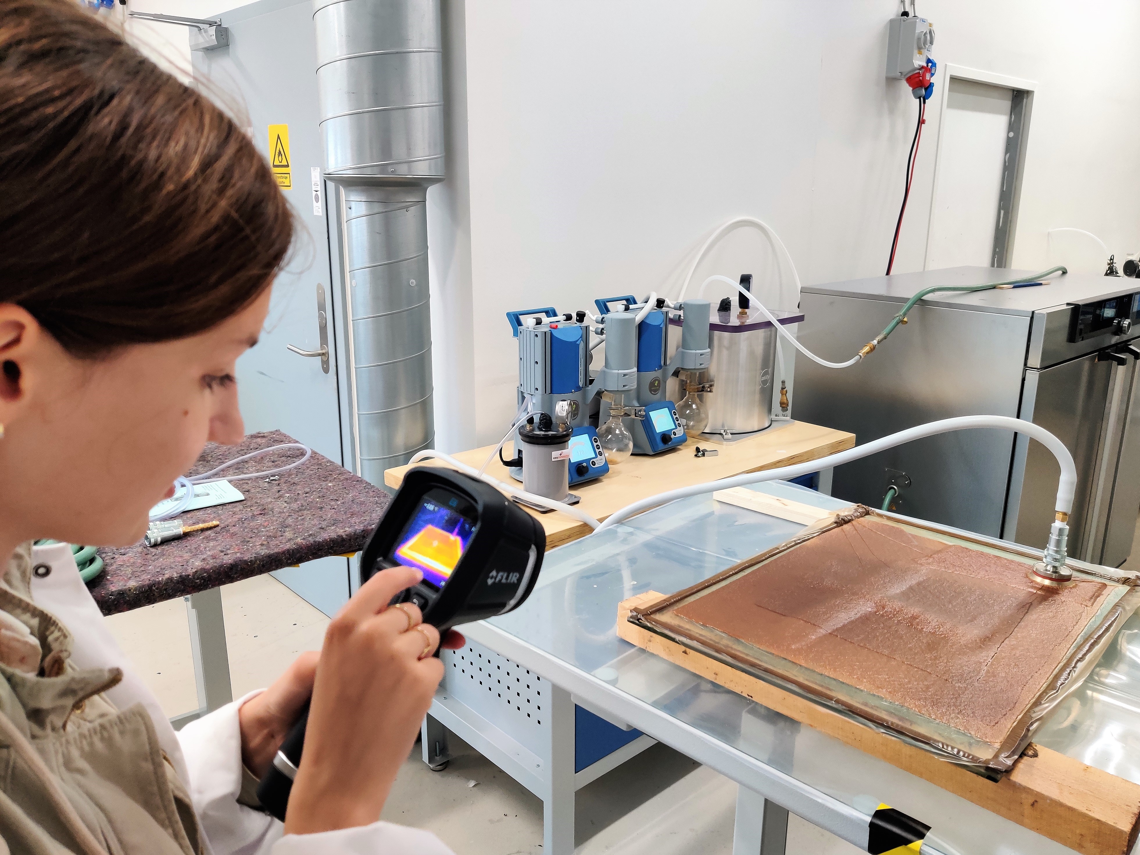 Studerende bruger FLIR-termisk kamera i laboratorie med infusionsudstyr Studerende bruger et FLIR-termisk kamera til at undersøge en laboratorieopstilling med infusionsudstyr og slanger på et arbejdsbord.