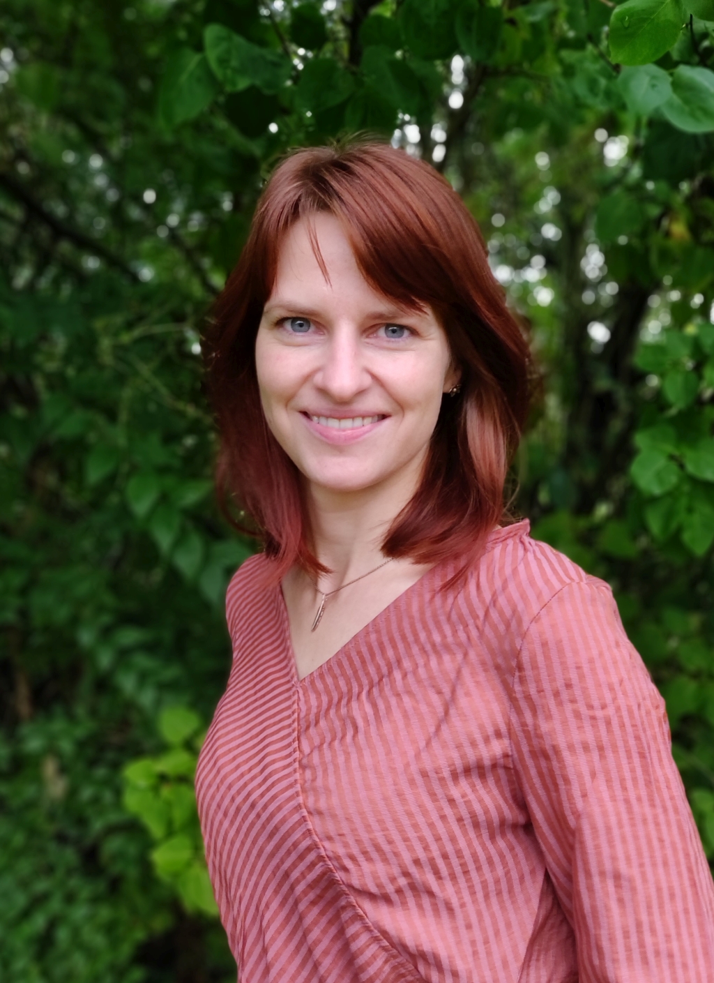 Franziska Eller smiling outdoors in front of green foliage, wearing a pink striped blouse.