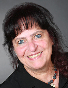 Portrait of a smiling woman with dark hair Smiling woman with dark hair and blue eyes in a studio portrait against a gray background.