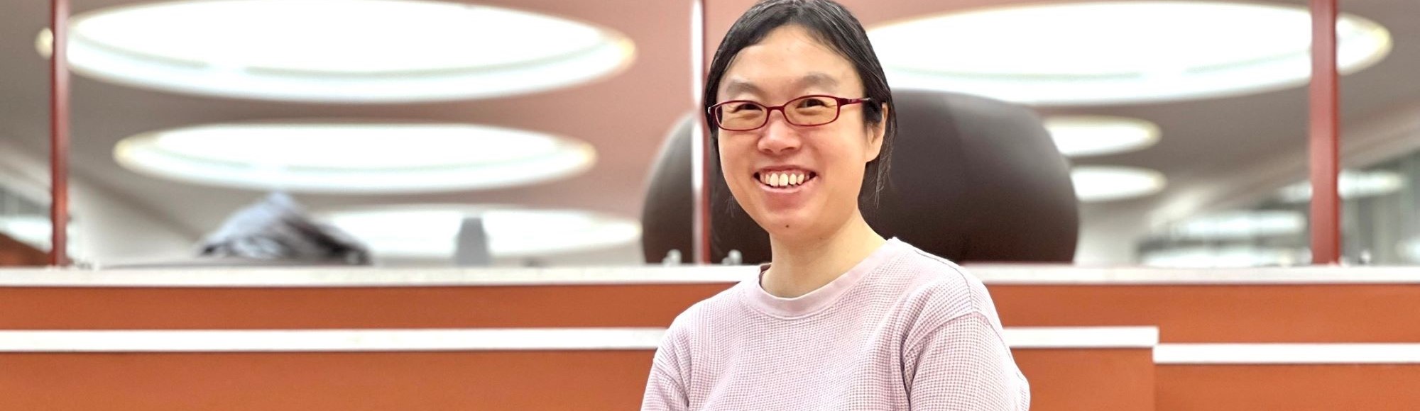 Zhengli Han smiling while seated indoors with circular ceiling lights in the background.
