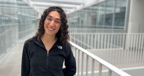Smiling woman in a black "THE NORTH FACE" jacket standing in a modern glass-lined corridor.
