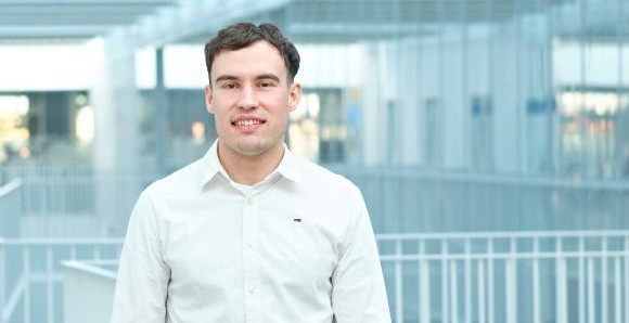 Smiling man in a white button-up shirt standing indoors against a bright modern interior background.