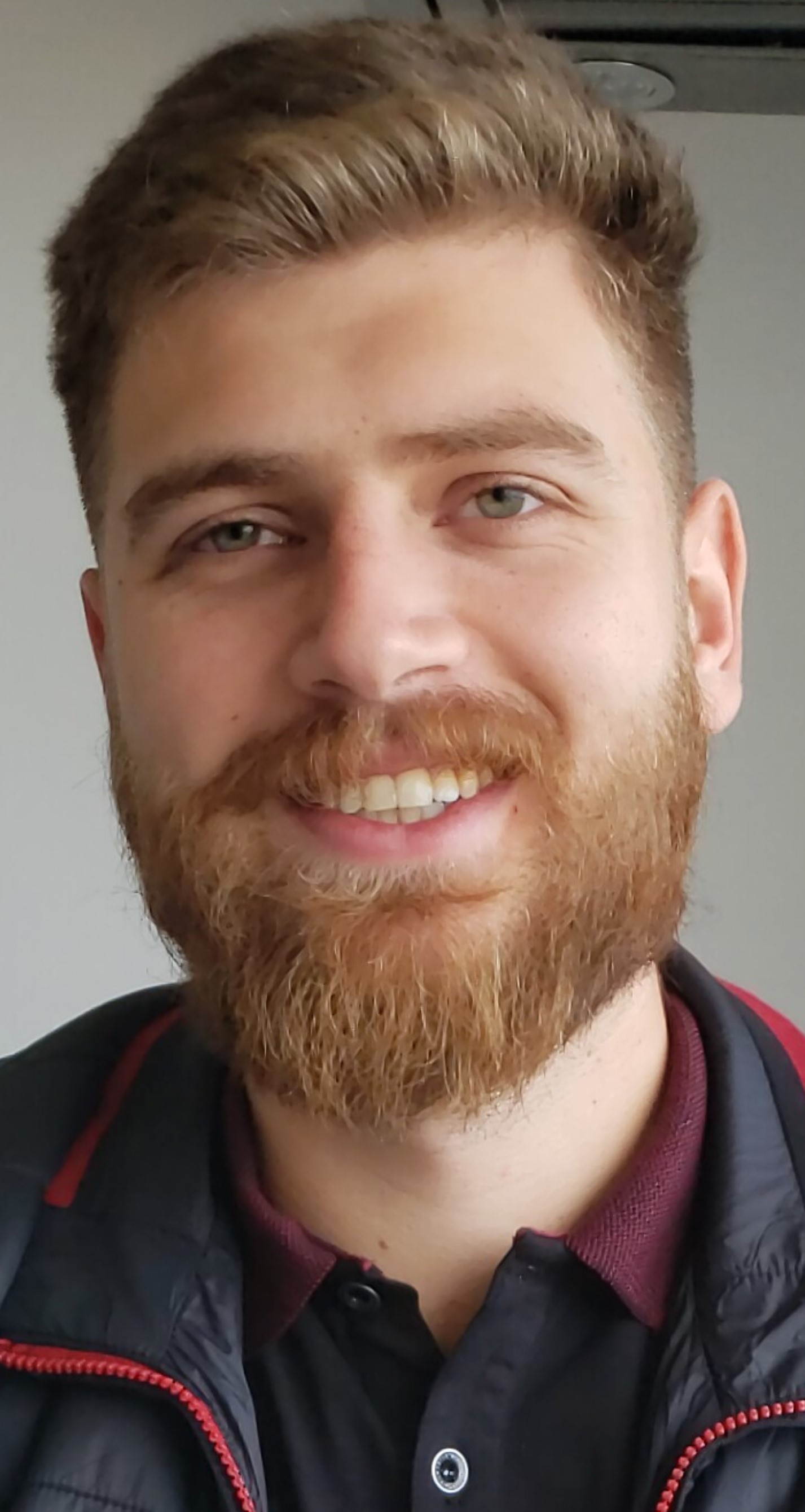 Close-up portrait of Henrique Raniro smiling indoors, wearing a dark jacket over a collared shirt.
