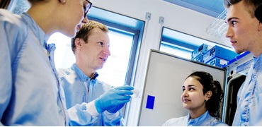 Lab team in protective clothing discussing work beside laboratory equipment.