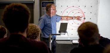 Presenter pointing at a projected concentric-circle diagram in front of an audience.