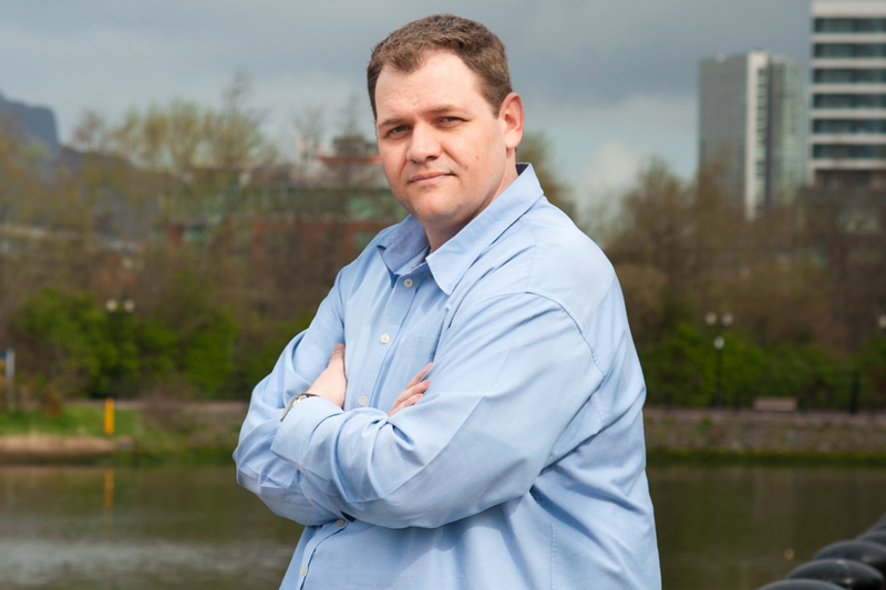 Panagiotis Manesiotis standing outdoors with arms crossed in a light blue shirt near water.