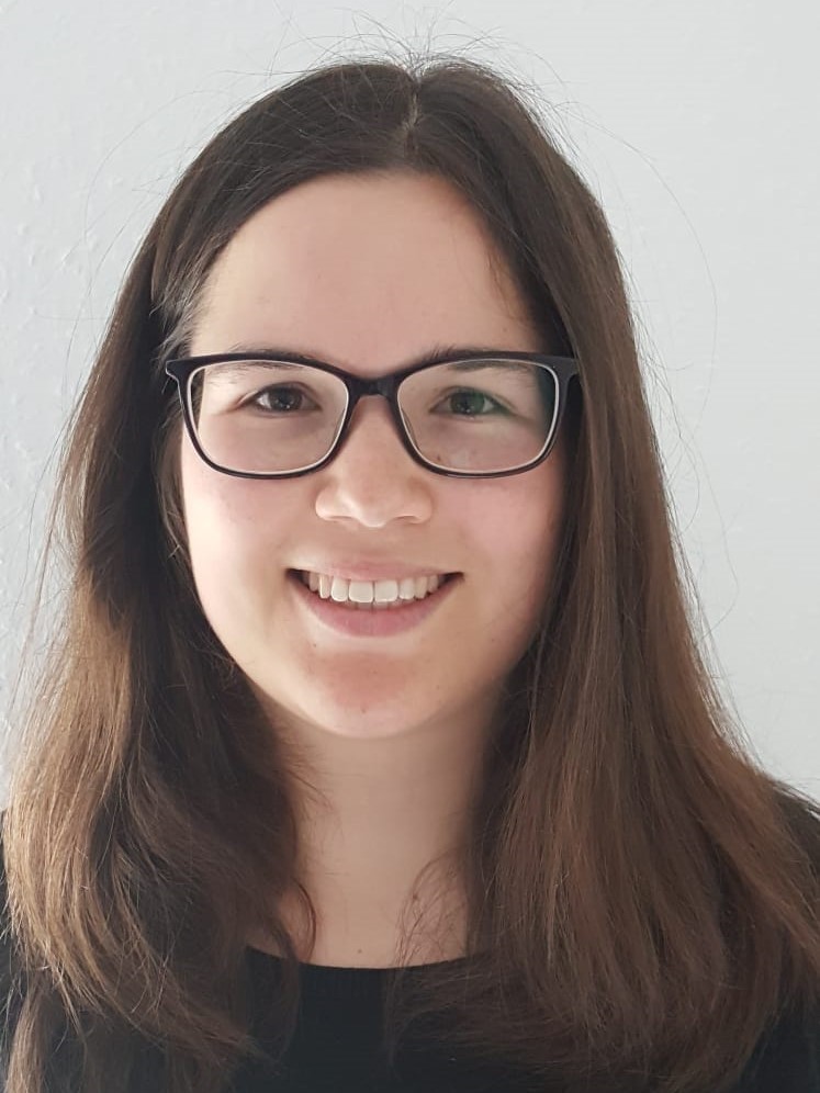 Portrait of Sophie Banke Sophie Banke smiling in a head-and-shoulders portrait with black rectangular glasses against a light gray background.