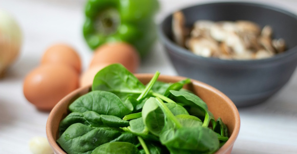 Spinach in a bowl. Four eggs, a green pepper and a bowl with mushrooms