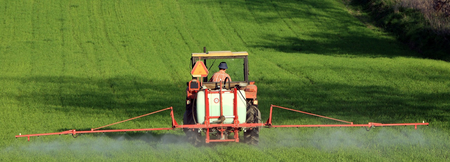 Traktor bagfra, der sprøjter en grøn mark med en bred landbrugssprøjte.