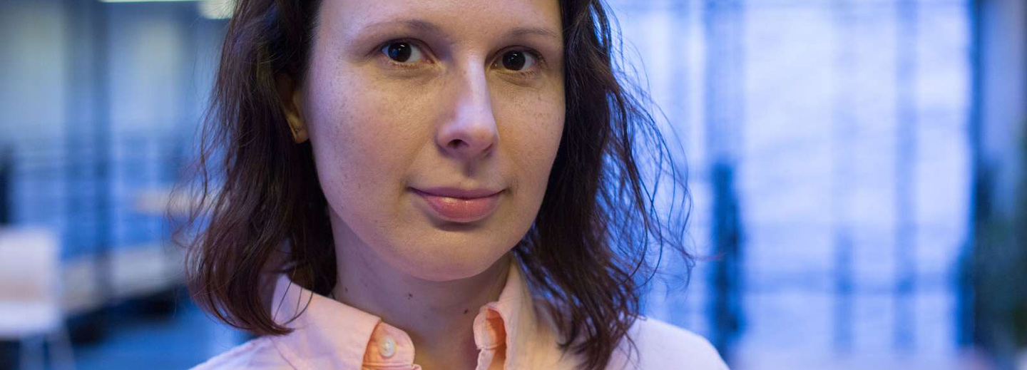 Nærbillede af en kvinde med mørkt hår og lys skjorte foran en sløret blåtonet baggrund.
