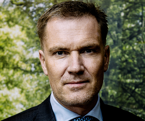 Portræt af Niels Thorborg i mørkt jakkesæt foran en grøn, sløret baggrund.