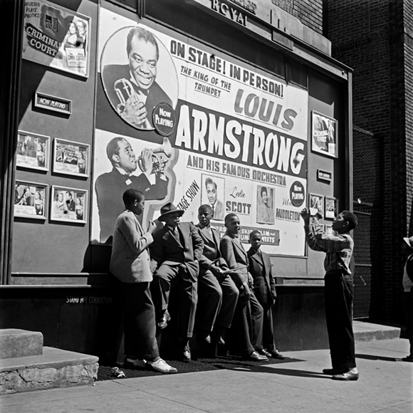 Seks unge afroamerikaner samlet foran en koncertplakat med Louis Armstrong 