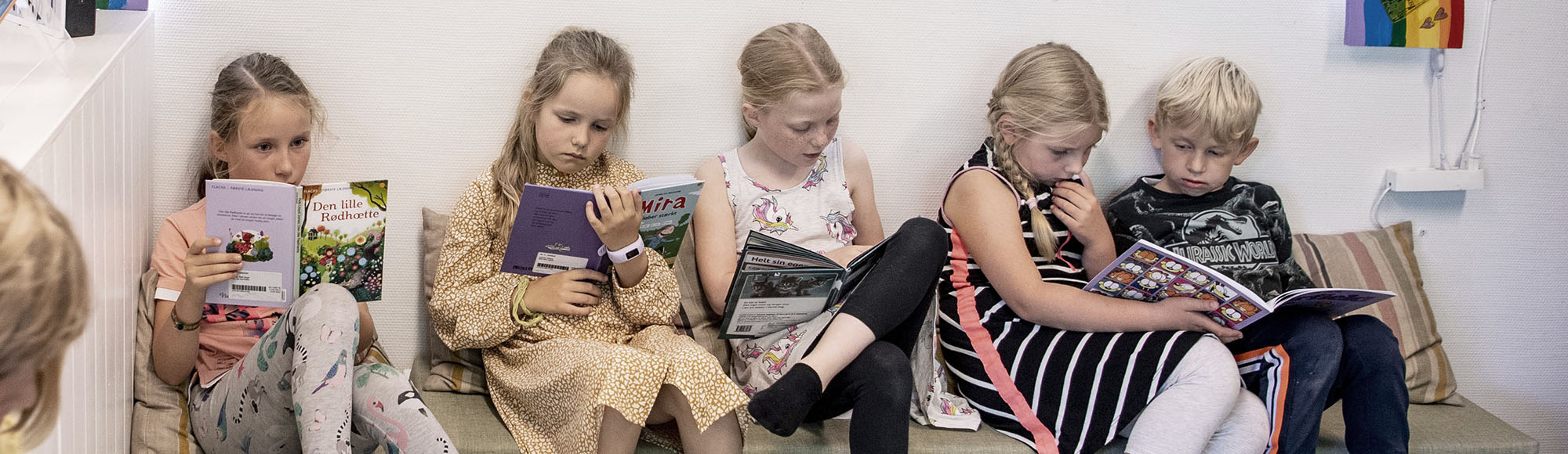 Fire piger og en dreng sidder i en sofa og læser biblioteksbøger.