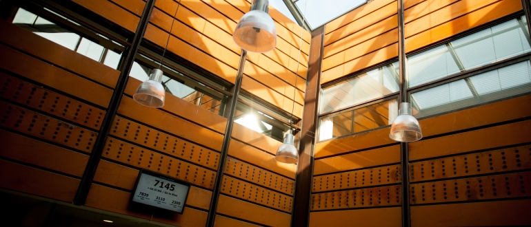 Modern building interior with wood-paneled atrium Modern atrium interior with wood-paneled walls, glass windows, hanging lights, and a sign reading "7145".