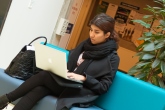 Person siddende på en turkis sofa med en bærbar computer i et indendørs miljø.