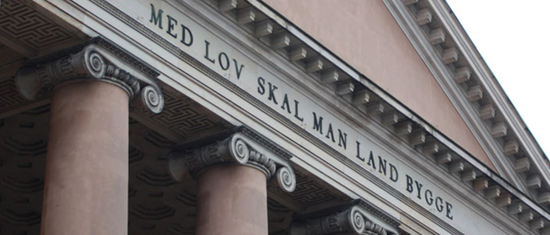 Klassisk bygning med teksten MED LOV SKAL MAN LAND BYGGE Klassisk bygning med søjler og teksten MED LOV SKAL MAN LAND BYGGE på facaden.