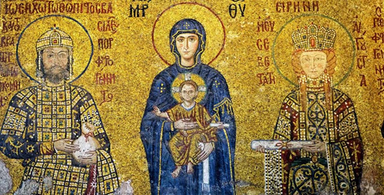Byzantine mosaic with three haloed figures in ceremonial dress, a central Madonna and Child, and Greek text on a gold background.