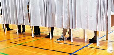 Borgere i gang med at stemme til kommunalvalg. Man kan se deres fødder under valggardinerne i en lokal gymnastiksal.