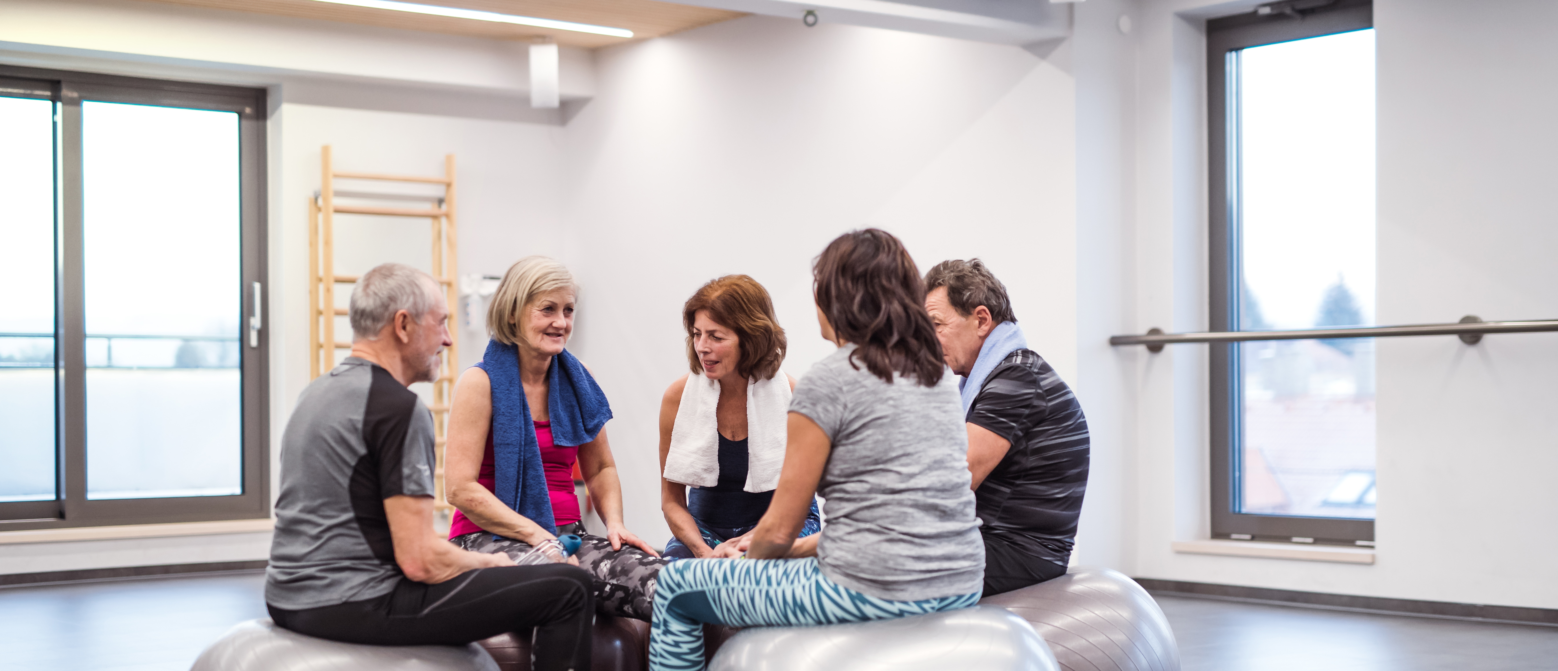 En gruppe sidder og hviler sig efter træning på store træningsbolde, mens de snakker sammen