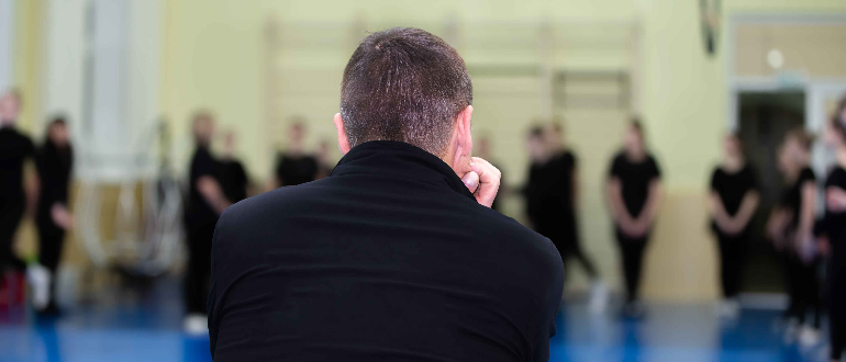 Ung mand sidder og kigger på idrætsfolk - set fra ryggen