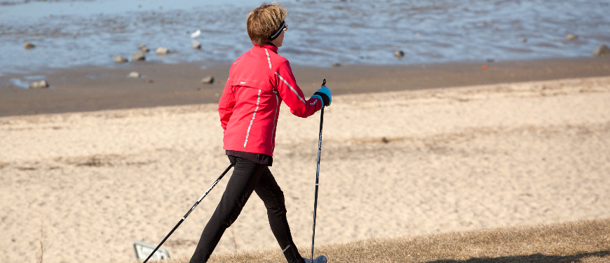 Kvinde går med vandrestave langs stranden
