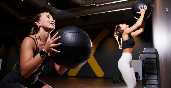 To unge kvinder træner med fitnessbolde op ad en væg