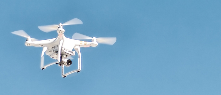 White quadcopter drone flying against a clear blue sky White camera drone hovering in a clear blue sky.