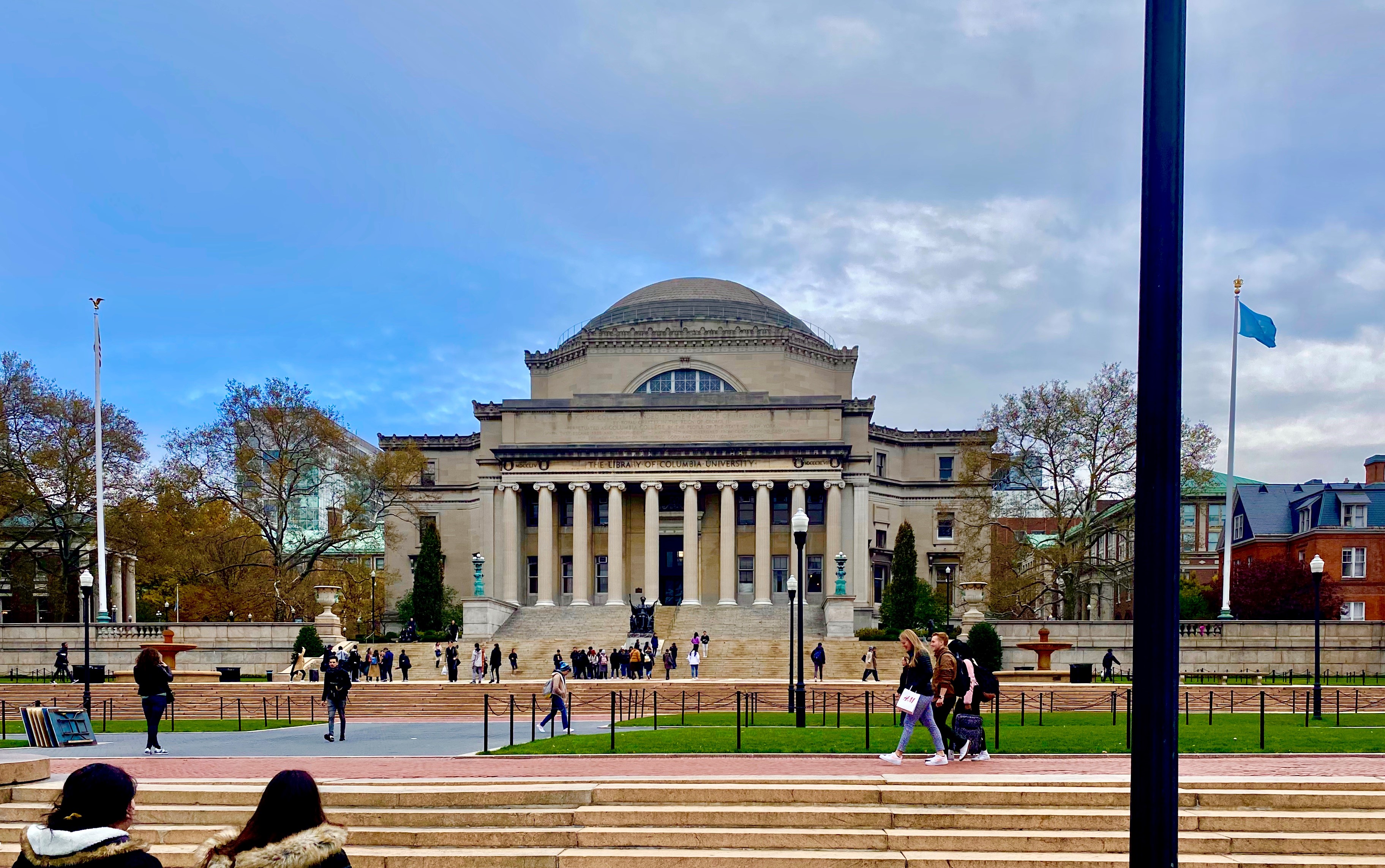Frontal view of a domed neoclassical university building with columns and steps, people on the plaza, and the text "THE LIBRARY OF COLUMBIA UNIVERSITY" on the facade.