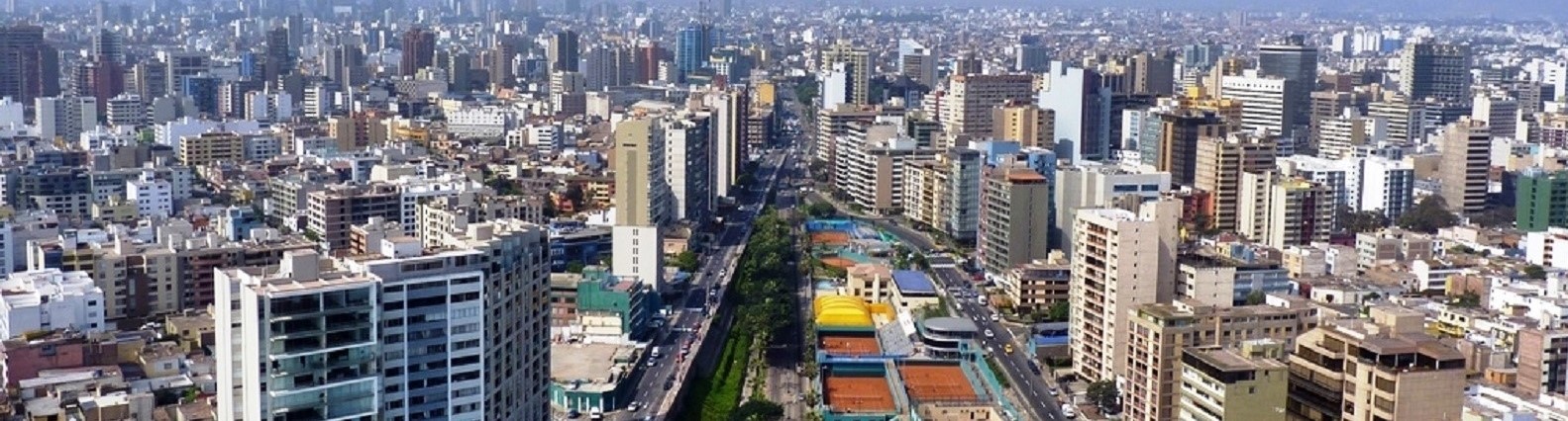 Aerial panoramic view of Lima, Peru with dense high-rise buildings, wide roads, and a central green corridor.