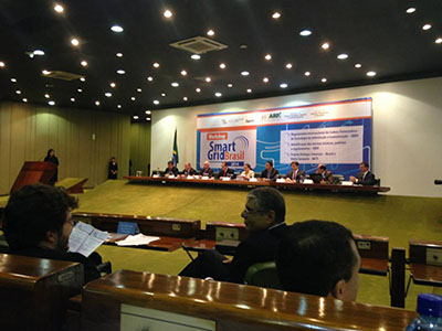 Conference hall with a panel discussion on stage and a large "Smart Grid Brasil" banner in the background.