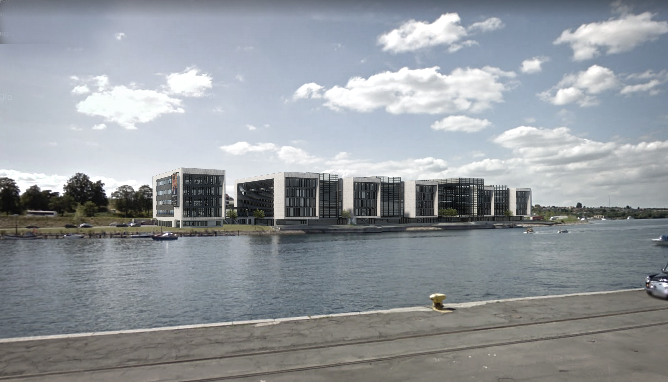 Moderne bygninger ved havnefronten set fra en kaj med vand i forgrunden og skyer på himlen.