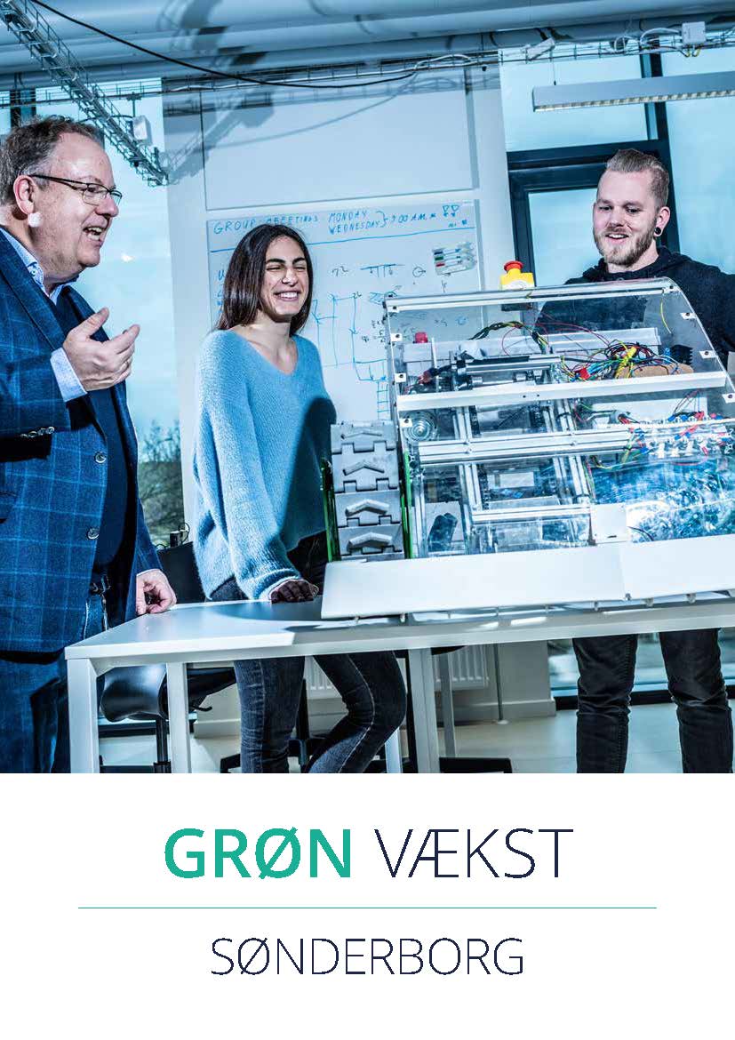Three people in a workspace looking at a technical machine on a table, with the text "GRØN VÆKST" and "SØNDERBORG" below.