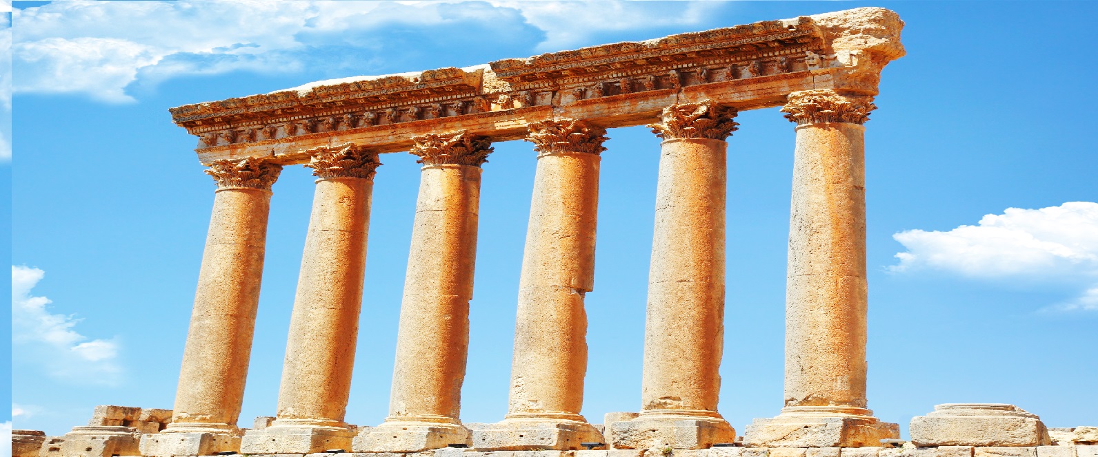 Ancient stone columns and a weathered entablature standing against a bright blue sky with clouds.