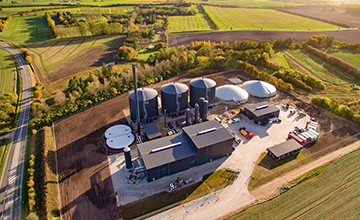 Aerial view of a Nature Energy biogas plant with tanks and domes surrounded by farmland.